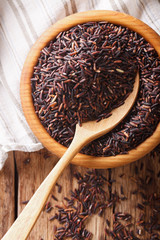 Raw wild black rice in a bowl close up. Vertical top view
