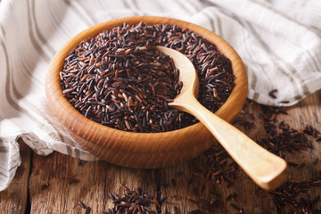 Healthy wild long black rice close up in a wooden bowl and spoon. Horizontal