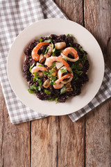 Paella from black rice with seafood close-up on a plate. Vertical top view