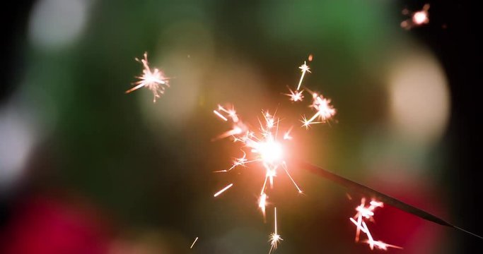 Burning sparkler refocusing decorated Christmas tree on background 4k close-up video. Firework flames sparks. Merry Christmas and Happy New year greeting card template