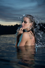 Fototapeta premium Portrait of sensual woman alone in infinity swimming pool over beautiful tropical and sunset sky background