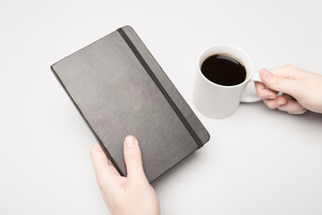 Hand is holding the notebook and coffee cup