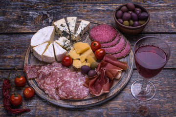 Red wine in a bottle, cork, bottle screw and a set of products - cheese, grapes, nuts, olives, figs on a wooden board, background