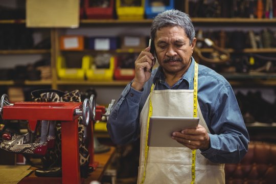 Shoemaker using tablet while phoning 