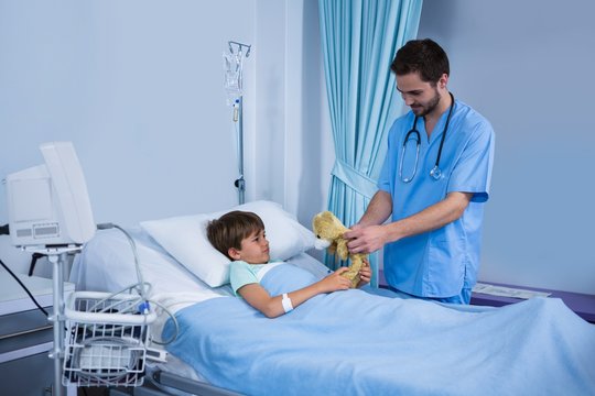 Male nurse giving teddy bear to patient during visit in ward