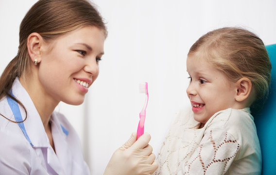 Surprised girl patient looking at toothbrush. Concept of teeth cleaning and hygiene education. 