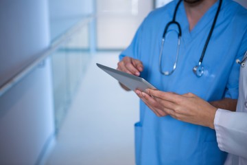 Mid section of doctor and nurse using digital tablet in corridor