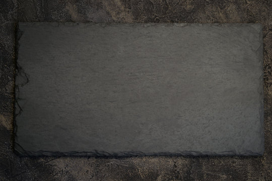 black slate board on dark stone background. Top view with copy s