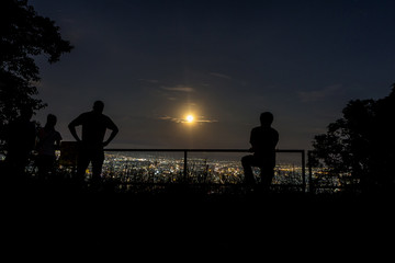 Fototapeta na wymiar people looking at full moon raising up in the sky over the city at night