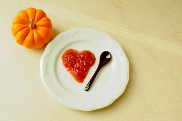Pumpkin and a plate with a portion of heart shaped jam on a marble surface