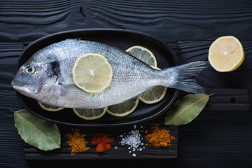 Raw dorado with various seasonings on a black wooden surface