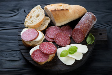 Baguette with salami and mozzarella over black wooden surface