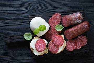 Salami and mozzarella bruschetta over black wooden surface