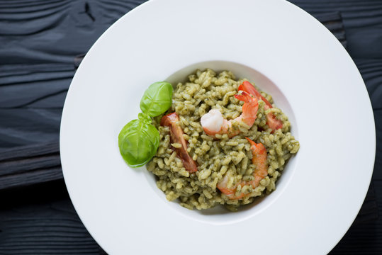 Spinach risotto with shrimps and tomatoes in a white glass plate