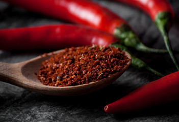 Spoon with seasoning chili and fresh chili on grunge dark background