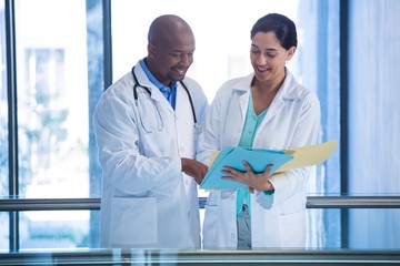 Male and female doctors having over file in corridor