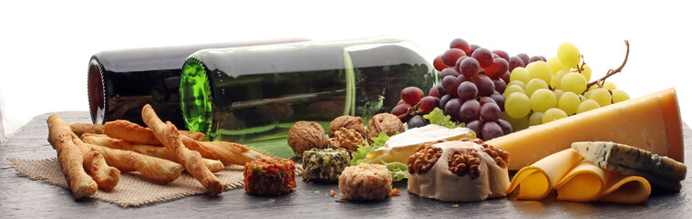 Assorted cheeses on round wooden board plate Camembert cheese, cheese grated bark of oak, hard cheese slices, walnuts, grapes, crackers, bread, thyme, dark black wood background