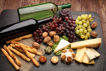 Assorted cheeses on round wooden board plate Camembert cheese, cheese grated bark of oak, hard cheese slices, walnuts, grapes, crackers, bread, thyme, dark black wood background