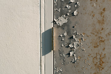 Metal hinge between the white wall and the old, rust and peeling paint steel door
