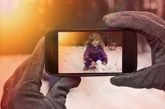 POV taking picture with smartphone. Baby playing in snow