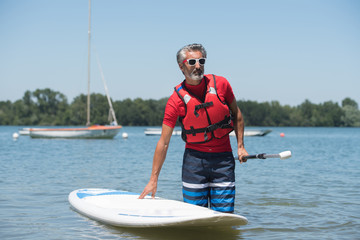 man next to a stand-up paddle board on the lake