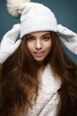 Beautiful girl in a white knitted hat with fur pompom. Model with gentle nude make-up. Cozy winter picture. Beautiful face.