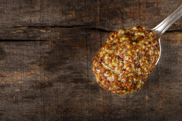 Silver spoon filled with mustard sauce with seeds and wine