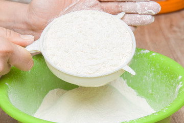 Hands with a sieve sift the flour into a bowl in the kitchen. Healthy eating and lifestyle.