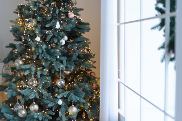 Christmas tree with decorations and lights in living room near the window