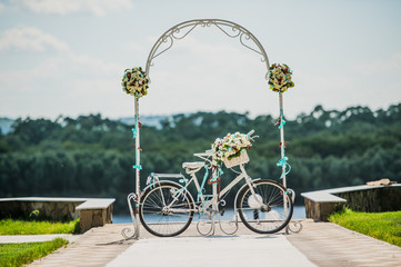 Fototapeta na wymiar White and blue arch decorated with flowers bycicle, wedding registration outdoors