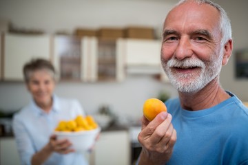 Senior man holding a bowl of apricot in kitchen