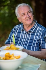 Senior man sitting at table with apricot fruits in bowl