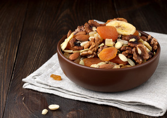 Dried fruits and nuts in brown bowl on wooden table.