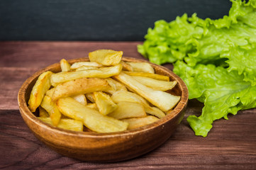French fries on a wooden plate with greens. Close-up