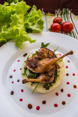 Roasted quail on a bed with mashed potatoes, rocket leaves and berry sauce.   white plate  wooden rustic background. Top view. Close-up