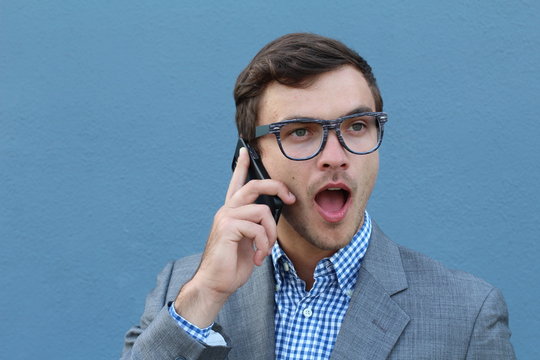 Young surprised man talking on his mobile phone isolated on blue background