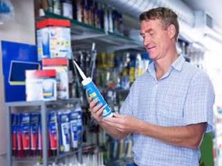cheerful man customer choosing sealant tube in hypermarket