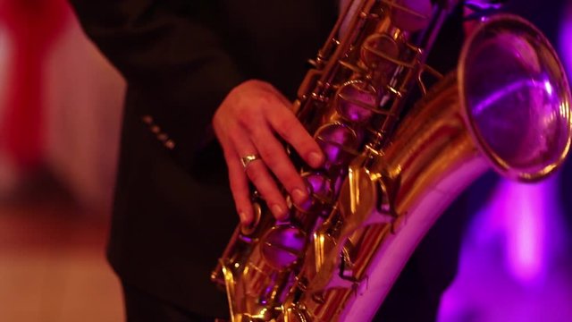 Musician is playing on saxophone in concert. Close-up on fingers pressing the keys of the instrument