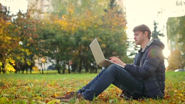 it startup programmer man working in the park using laptop sitting on the grass in sunny autumn day
