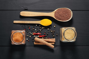 Ground spices in bottles with spon, papper, cinnamon on black wooden background. Top view