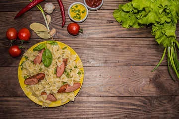 Grilled sausage with pasta, slices of bread, herbs and cherry tomatoes. On a wooden rustic brown background. Top view. Close-up