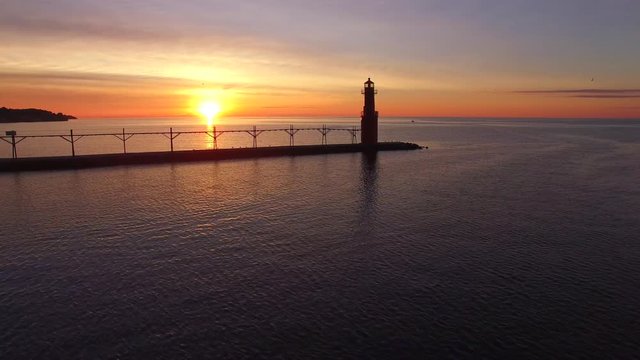 Dramatic Lake Michigan sunrise over harbor with lighthouse.
