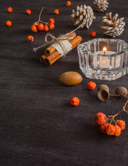 Dark Christmas background with candles and berries of mountain ash. White pine cones and branches with acorns. Cinnamon tied with string. Top view angle of 45 degrees.