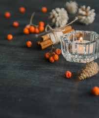 Dark Christmas background with candles and berries of mountain ash. White pine cones and branches with acorns. Cinnamon tied with string. Top view angle of 45 degrees.