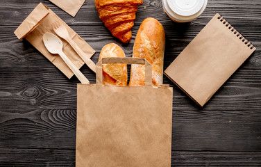 cup coffee and bread in paper bag on wooden background