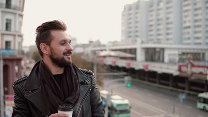 happy stylish handsome man with a beard drinking takeaway coffee or tea looking to the side.