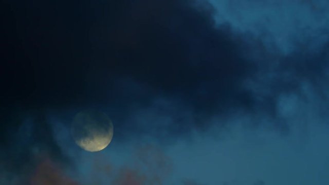 Moon rising as dark clouds rush past, time lapse.
