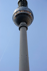 Fototapeta na wymiar Fernsehturm Berlin / Die Untersicht auf den Berliner Fernsehturm vor einem blauen Himmel mit Kondenstreifen.