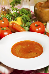 Red fish soup in a white plate beside fresh vegetables.