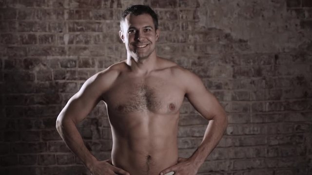 Muscular and fit mature bodybuilder posing demonstrates the core muscles. Isolated on brick background.